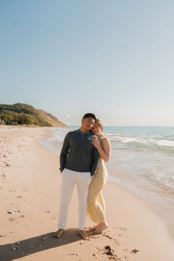 Couple posing close together along the shoreline at Empire Beach after their Sleeping Bear Dunes proposa.