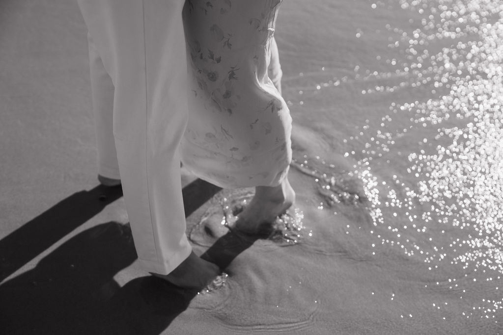 Close up black and white photo of the couples toes in the sand along the shoreline at Empire Beach.