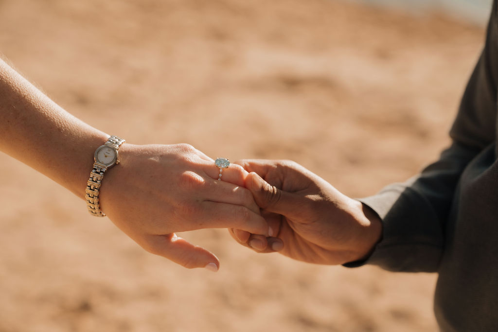 Close up shot of a couple caressing hands and showing off an engagement ring after a Sleeping Bear Dunes proposal.