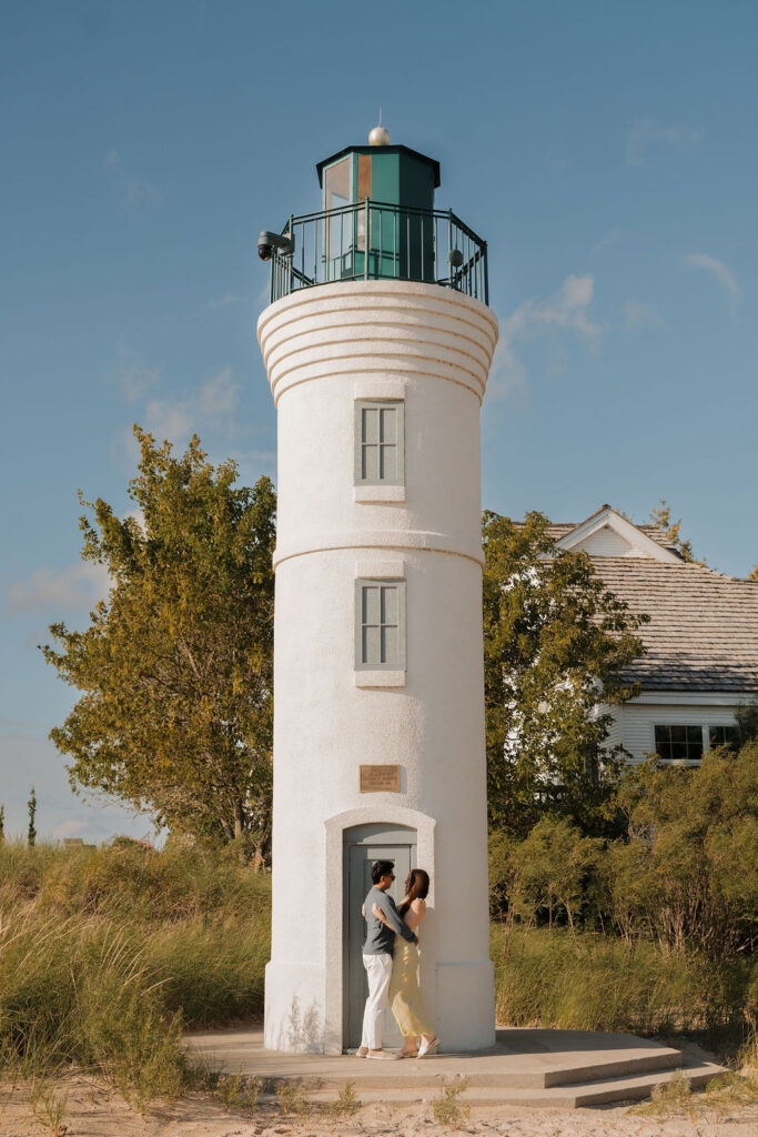Couple hugging in front of Robert H. Manning Memorial Lighthouse on Empire Beach.