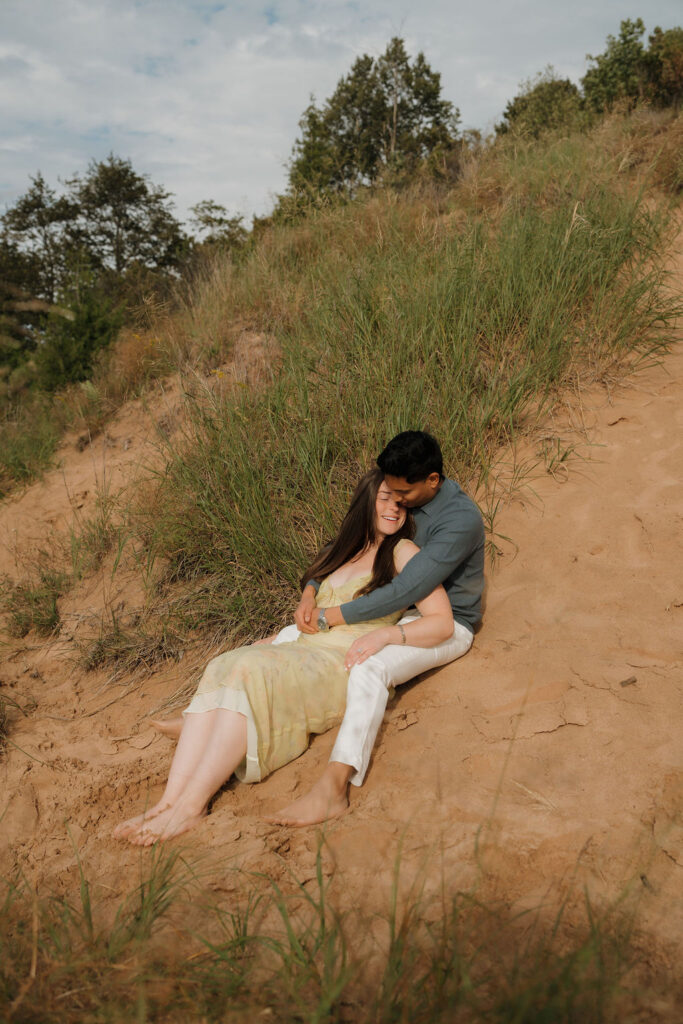 Couple laying in the sand of the dunes at Empire Bluff for their Sleeping Bear Dunes proposal.