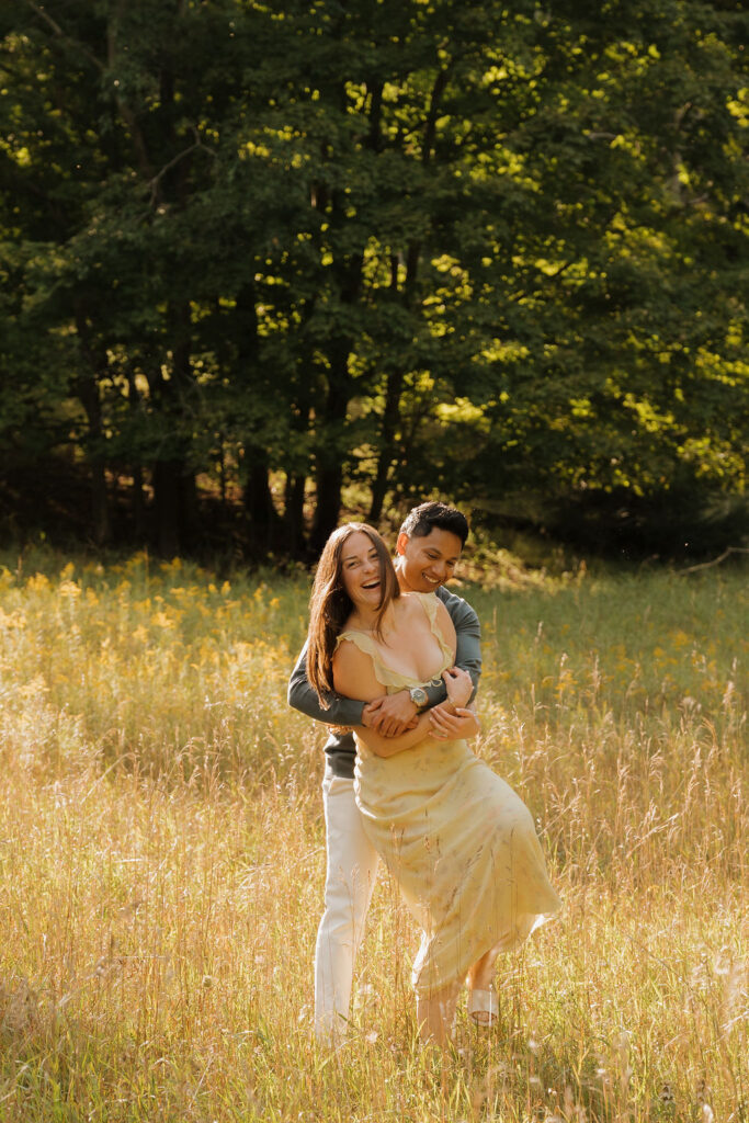 Man twirling his fiancé around in a field during golden hour.