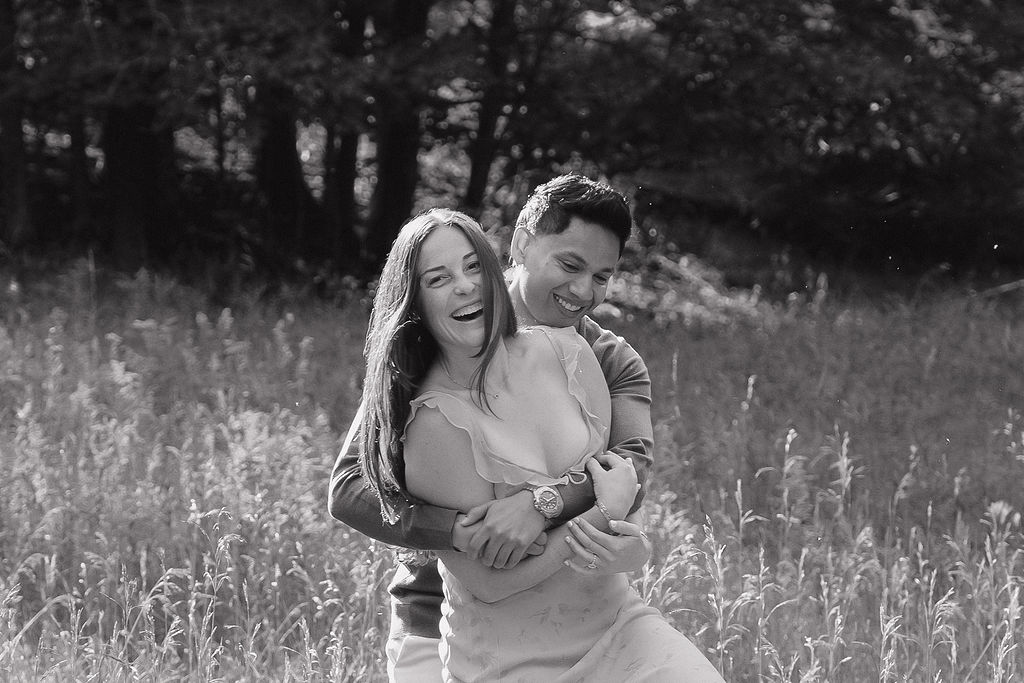 Black and white close up shot of a man twirling his fiancé around during golden hour in a field.