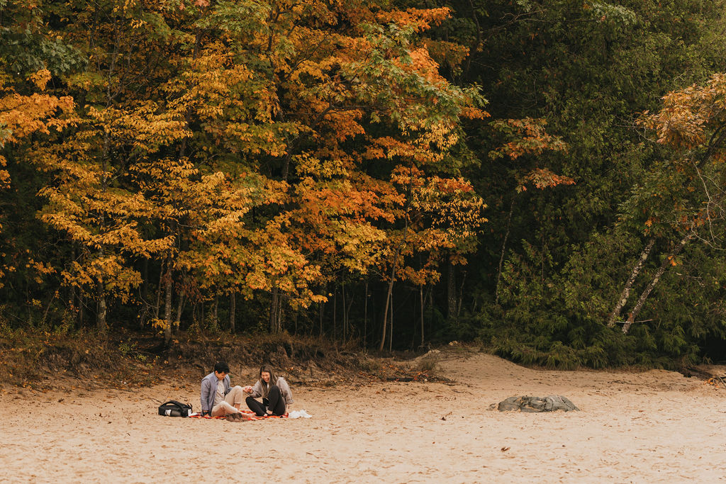 Couple sitting in the sand on a blanket at Old Mission Lighthouse during the fall.