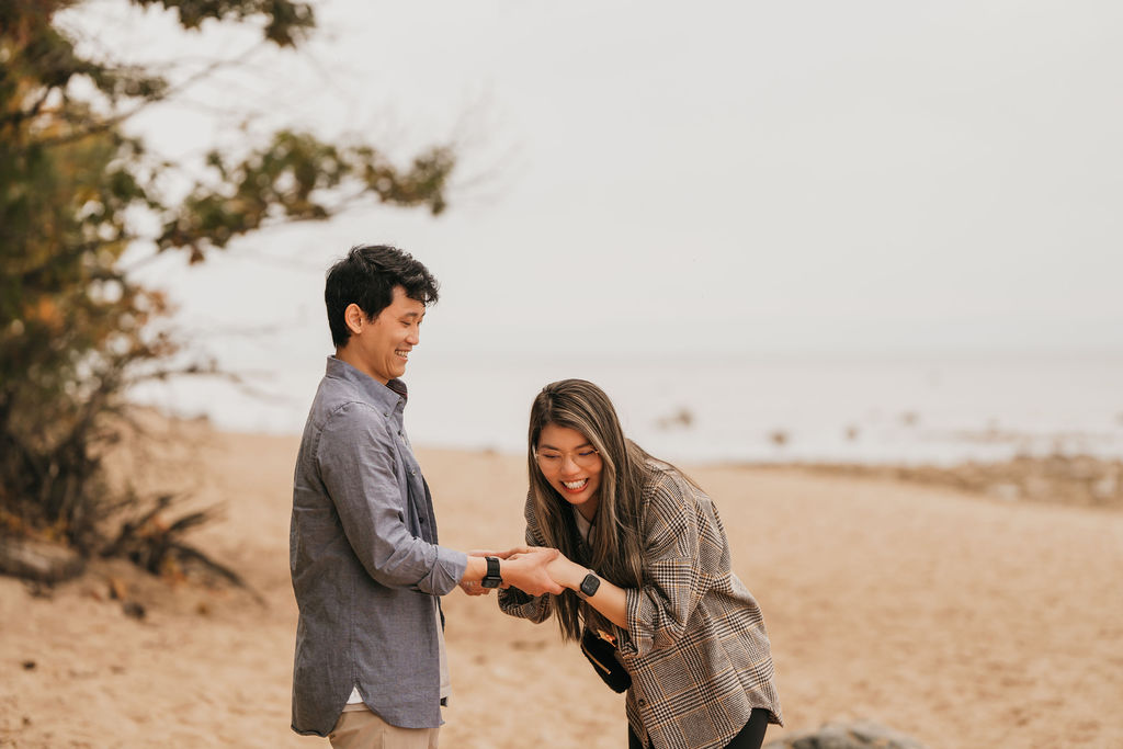 Couple laughing at Old Mission Lighthouse during their Traverse City Michigan proposal on the beach.