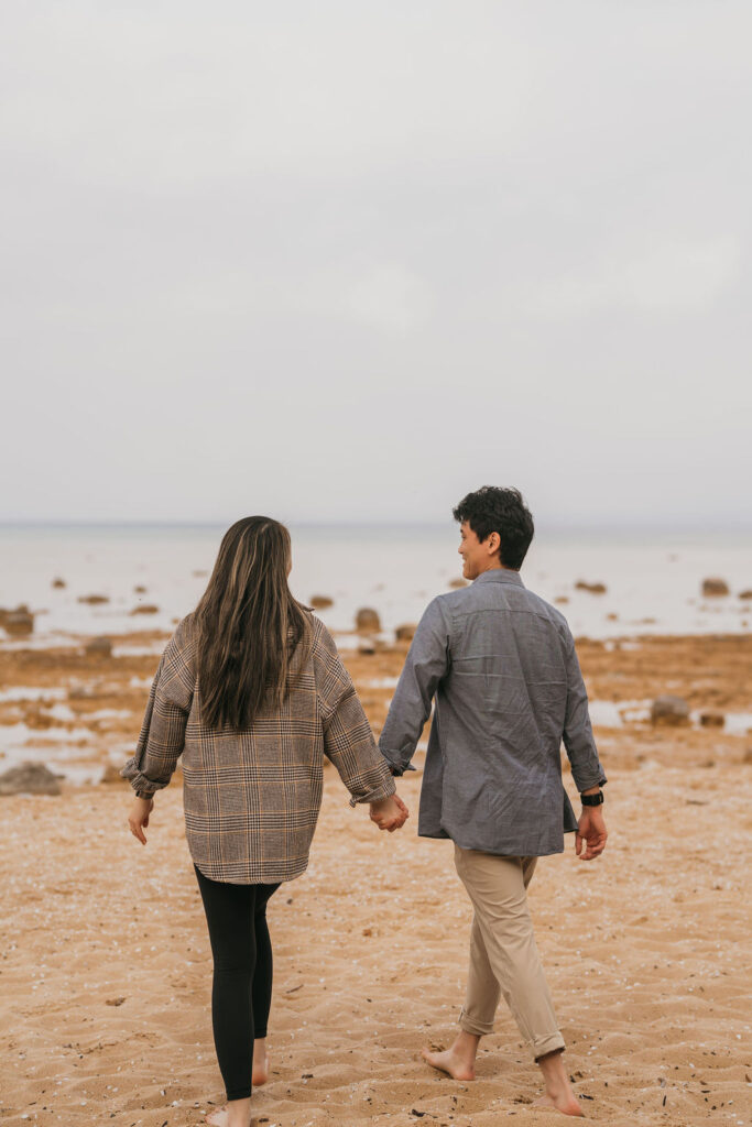Couple holding hands and walking on the beach for their Traverse City Michigan proposal photos
