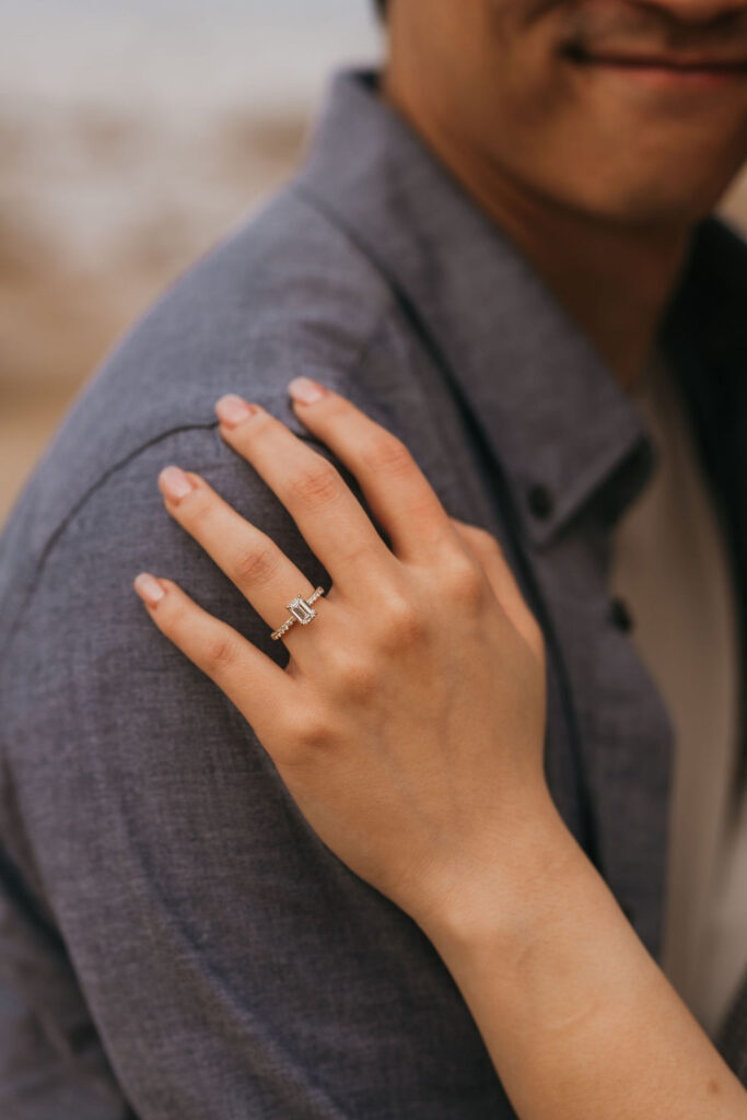 Close up detail shot of a woman resting her hand on her fiancés shoulder with her engagement ring.