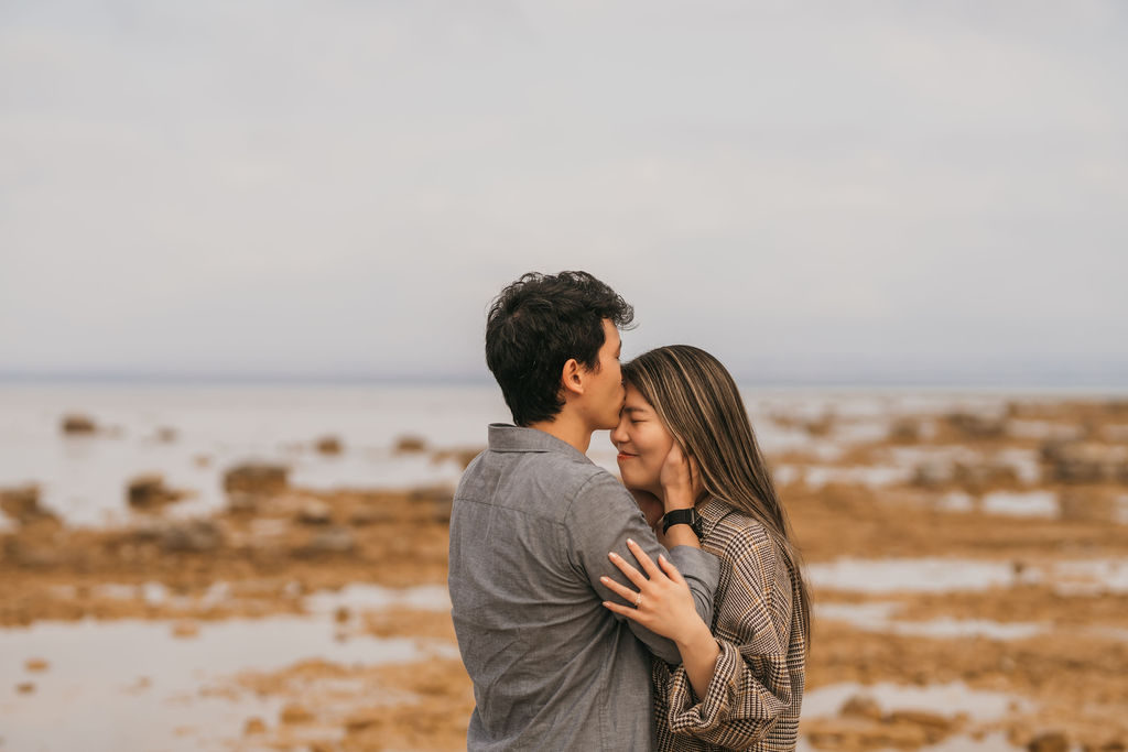 Man kissing his fiancés forehead on the beach during their Traverse City Michigan proposal.