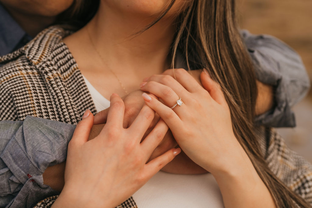 Close up shot of a couple holding hands showcasing an engagement ring.