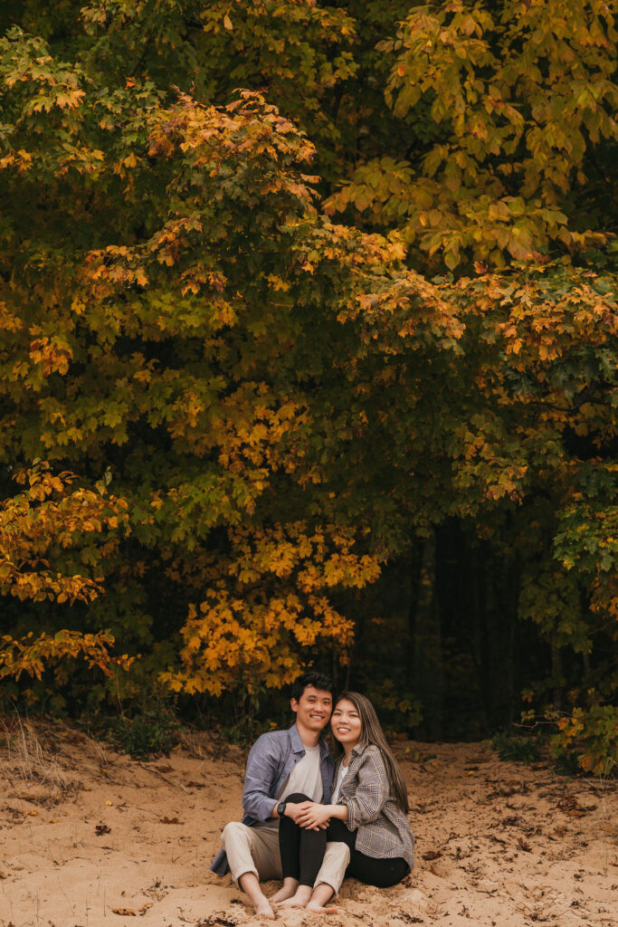 Couple sitting in the sand during their fall Northern Michigan proposa.