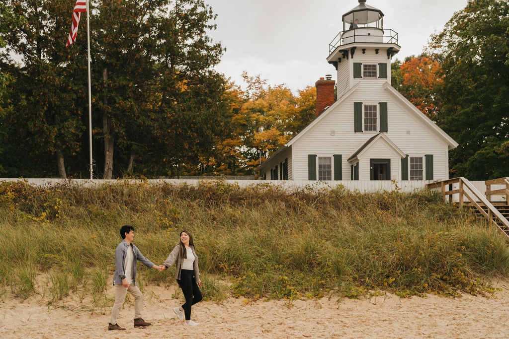Couple walking hand in hand in front of Old Mission Lighthouse for their Traverse City Michigan proposal photos during the fall.