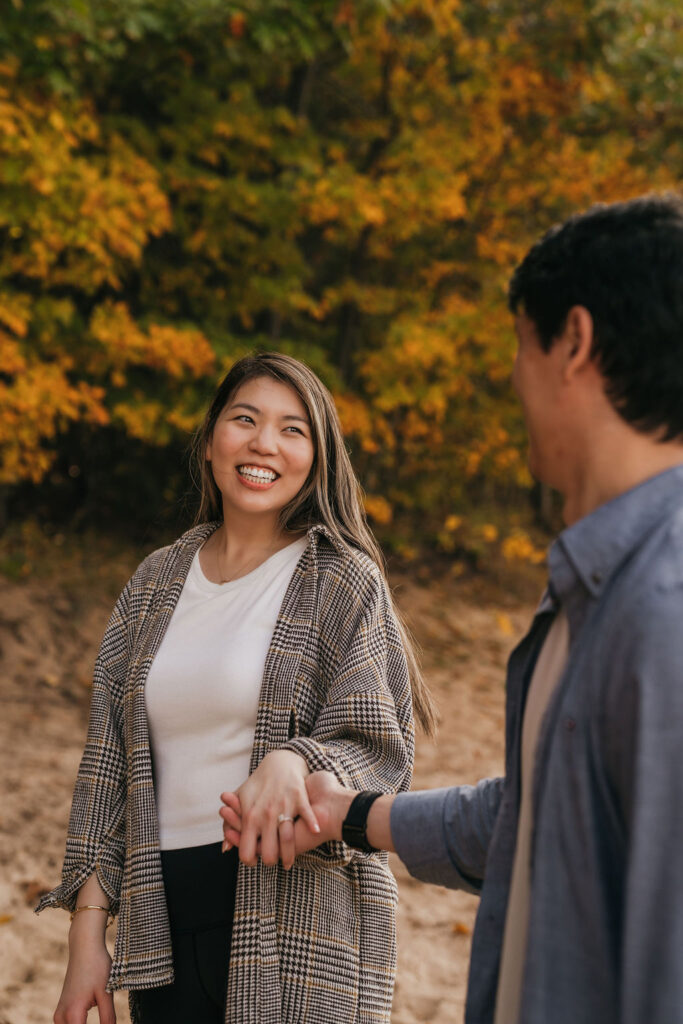 Couple holding hands and smiling on the beach during fall.