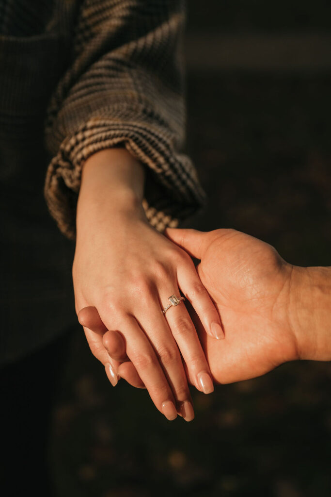 Close up shot of a couple holding hands and showing off the woman's engagement ring during golden hour.