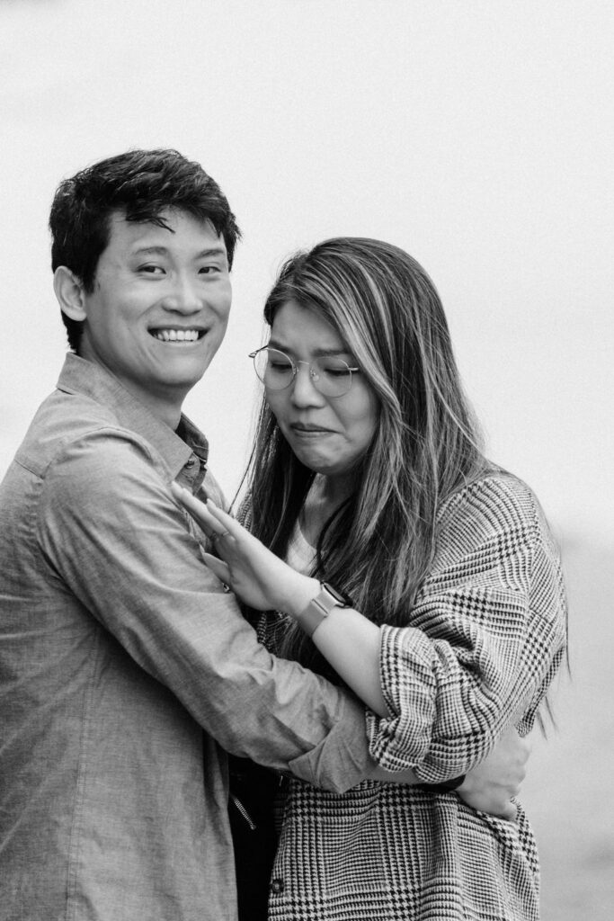 Black and white photo of a woman getting emotional as she looks down at her new engagement ring.