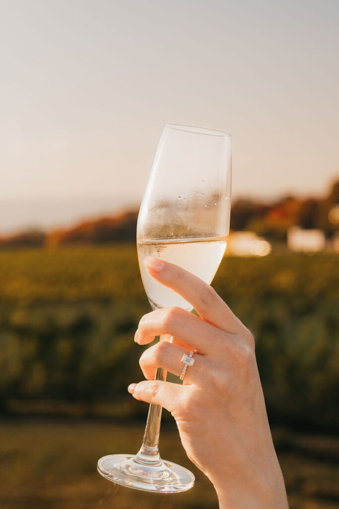 Close up shot of a woman holding a champagne glass and showing off her engagement ring.