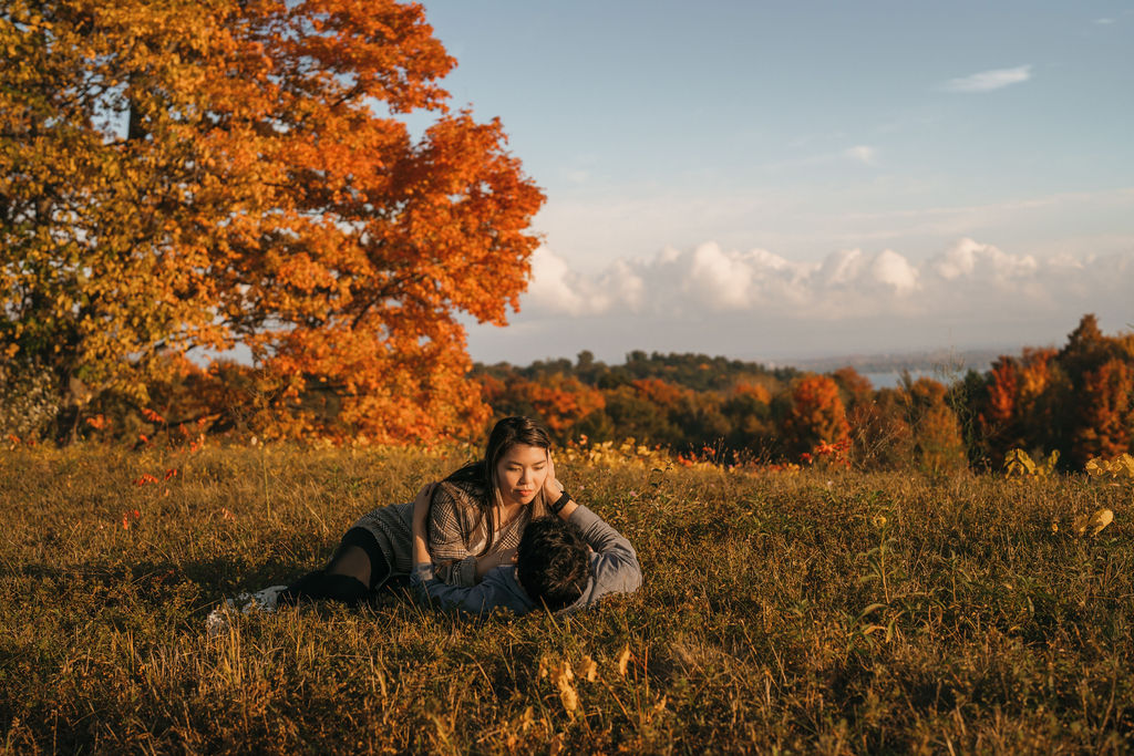 Couple laying in the field together at The Overlook with warm fall colors behind them.