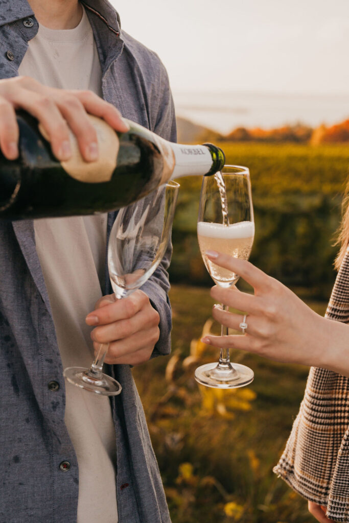 Close up of a man pouring his fiancé champagne to celebrate their proposal.