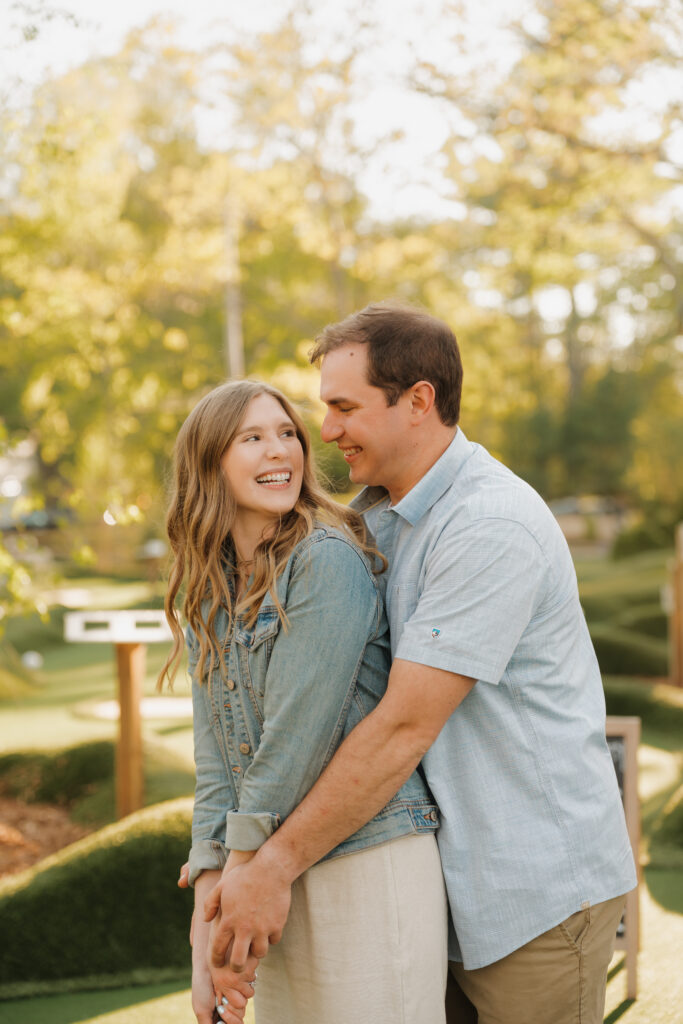 fiance holding the club with his wife and celebrating their engagement with mini-golfing