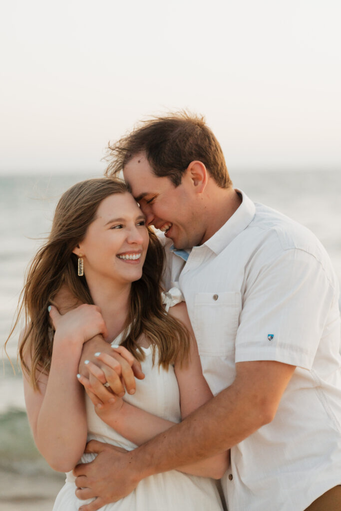bride and groom holding each other close and smiling happily during their engagement session