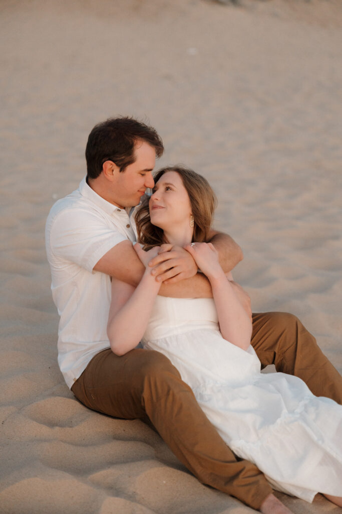 couple sitting in the sand at empire beach looking at each other lovingly