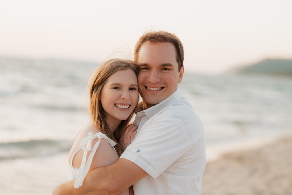 soon to be bride and groom smiling happily at the camera during their engagement session at sleeping bear dunes